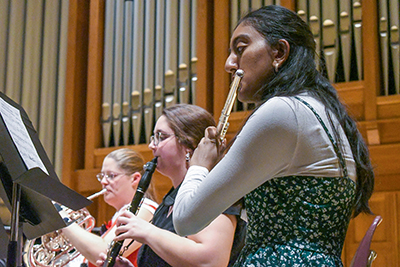 A student playing flute alongside a clarinetist and French horn player during a music ensemble performance in Gano Chapel.