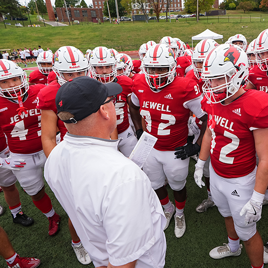 Football team wearing helmets and jerseys gathered around their coach.