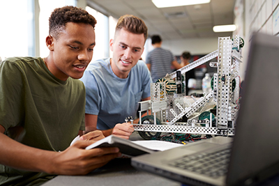 2 male students working together with a laptop to assemble a metal robotics project in a classroom.