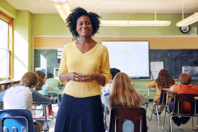 A female teacher smiling in front of her class in an elementary classroom setting.