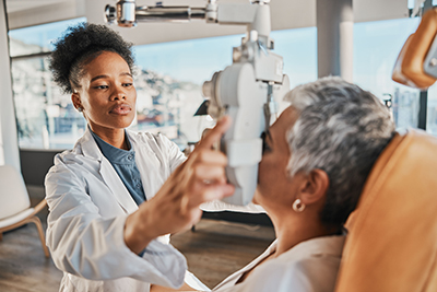 An optometrist in a white lab coat using vision testing equipment to perform an eye exam on a patient.