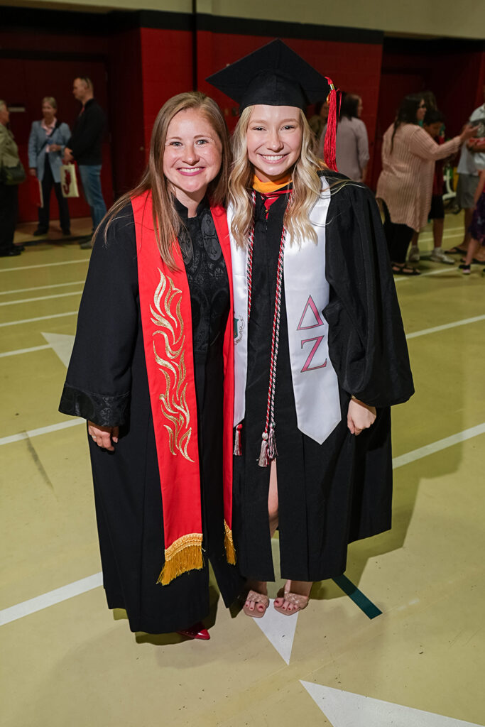 Chaplain Melissa Bryson Dowling smiling alongside a graduating student wearing a cap, gown, and fraternity stole.