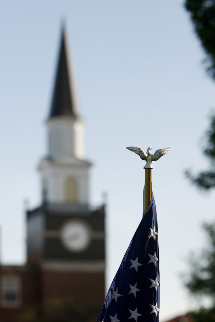 eagle emblem on top of American flag with Jewell chapel steeple in background
