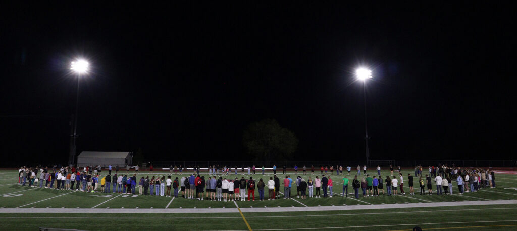 students in circle on football field praying at faith event