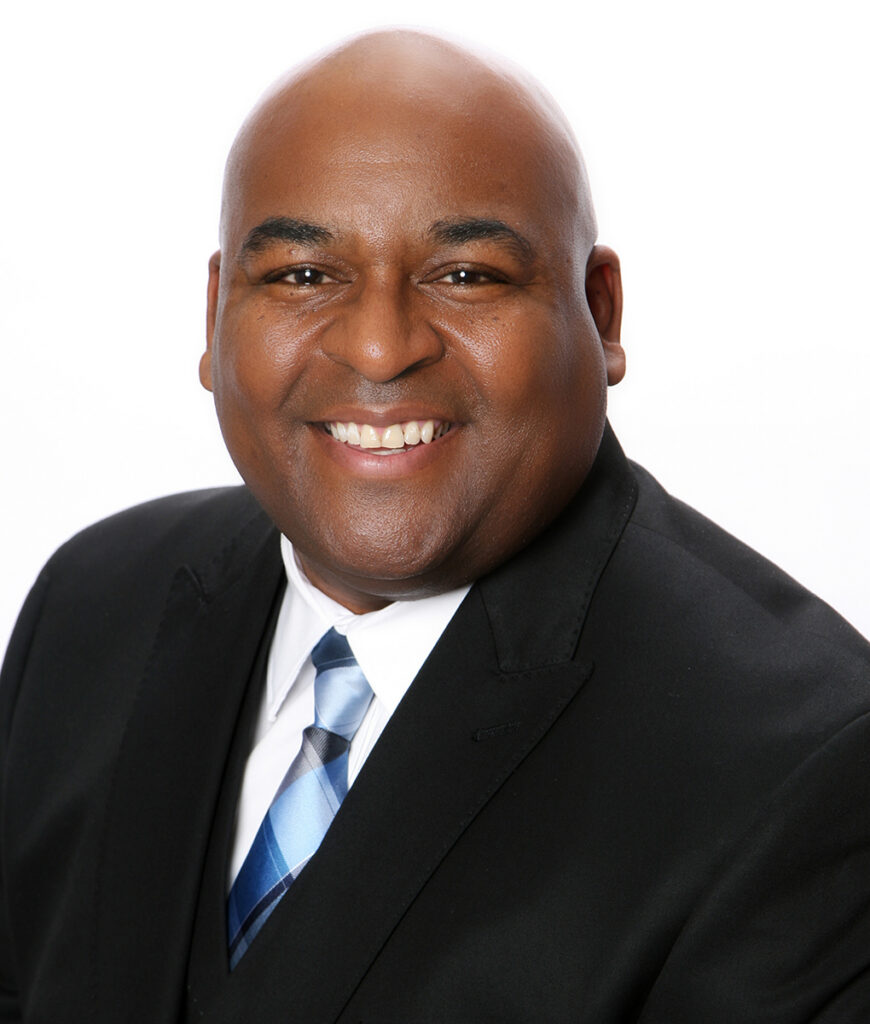 Reverend Dr. Vernon Howard, Adjunct Instructor and Lecturer in the Core Curriculum and Center for Faith and Culture, smiling in a black suit and blue tie.