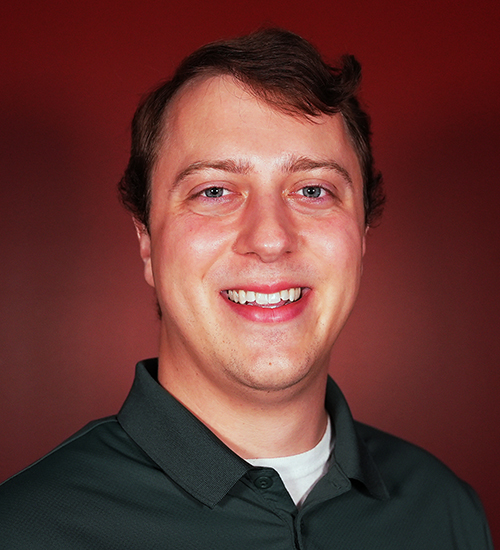 Anderson Fitch, Assistant Professor of Psychology at William Jewell College, smiling in a dark green polo shirt against a red backdrop.
