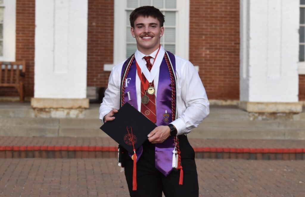 Ford Brandt, a male graduate wearing academic stoles, honors medals, and a tie, holding his mortarboard cap outside Jewell Hall.