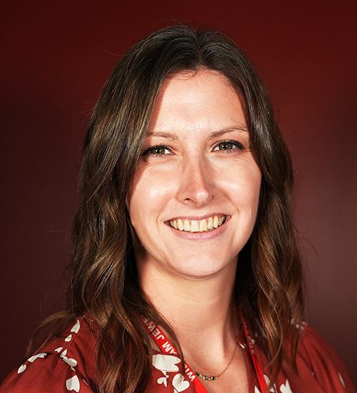 Allison (O'Leary) Lassiter, Assistant Professor of Practice in Education at William Jewell College, smiling in a red patterned top against a dark red backdrop.