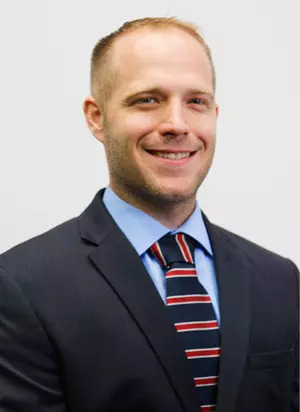 Ryan Arens, Assistant Athletic Trainer, smiling in a dark suit, light blue shirt, and red-and-blue striped tie.