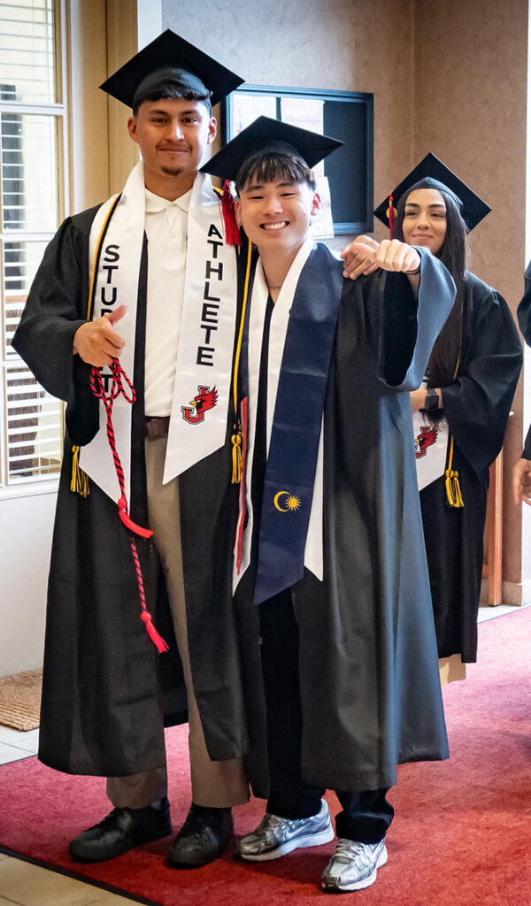 two male graduates in caps and gowns giving thumbs up