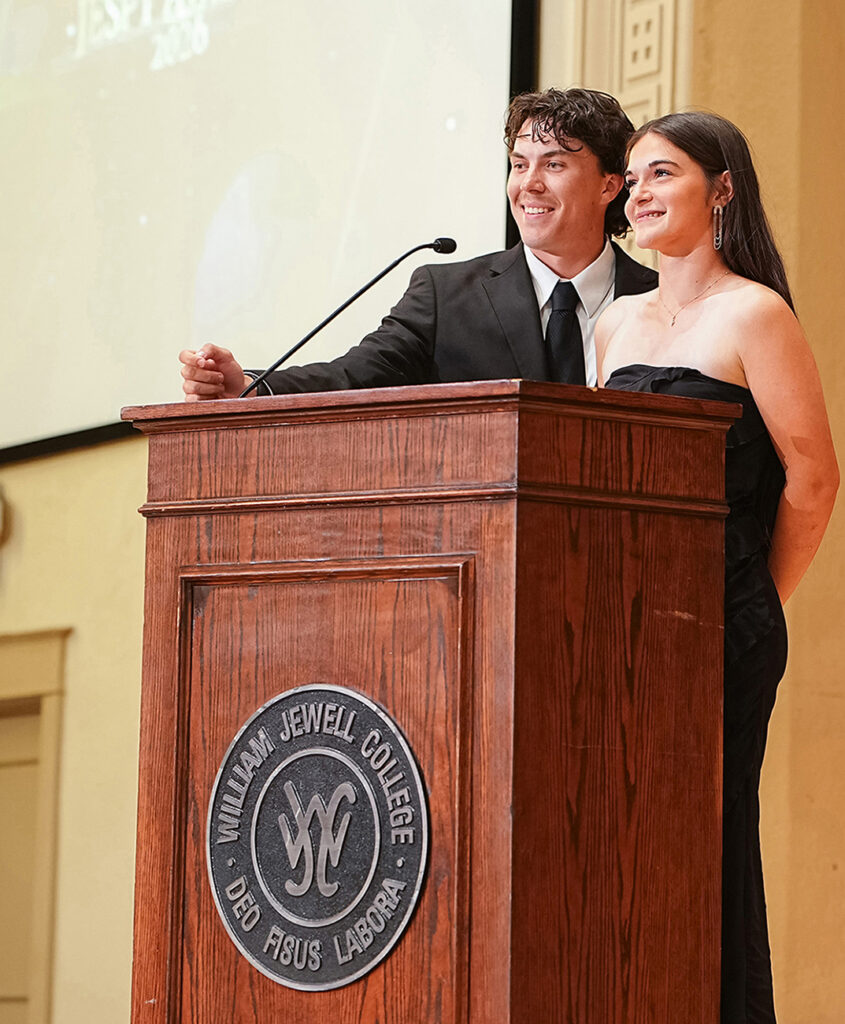 2 student on stage at podium making announcement during awards ceremony