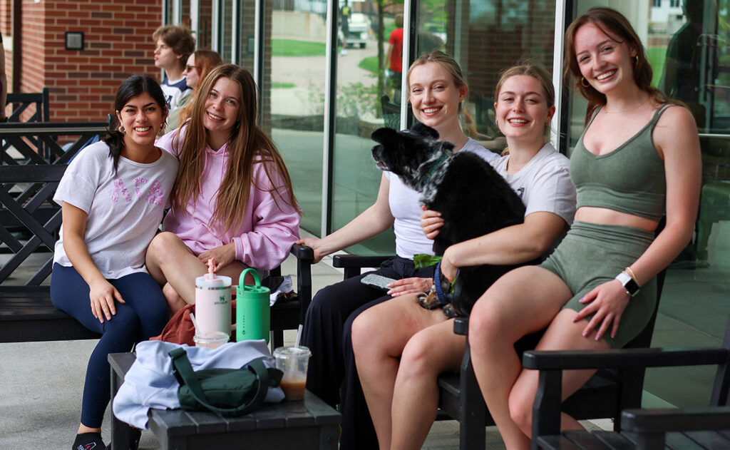 girls sitting in front of campus building holding a dog