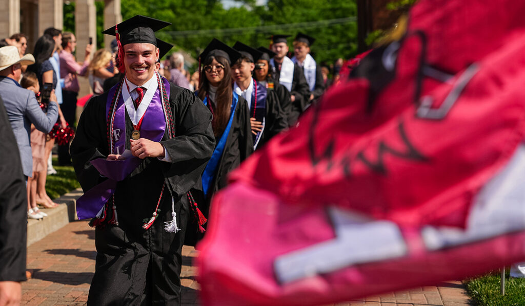 line of students walking wearing graduation caps, gowns, honors cords