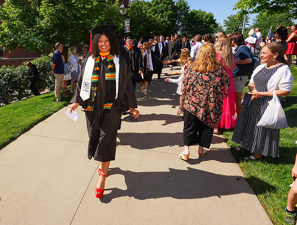 woman in graduation cap and gown walking on campus on graduation day