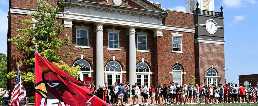 new students lined up outside behind flag bearers