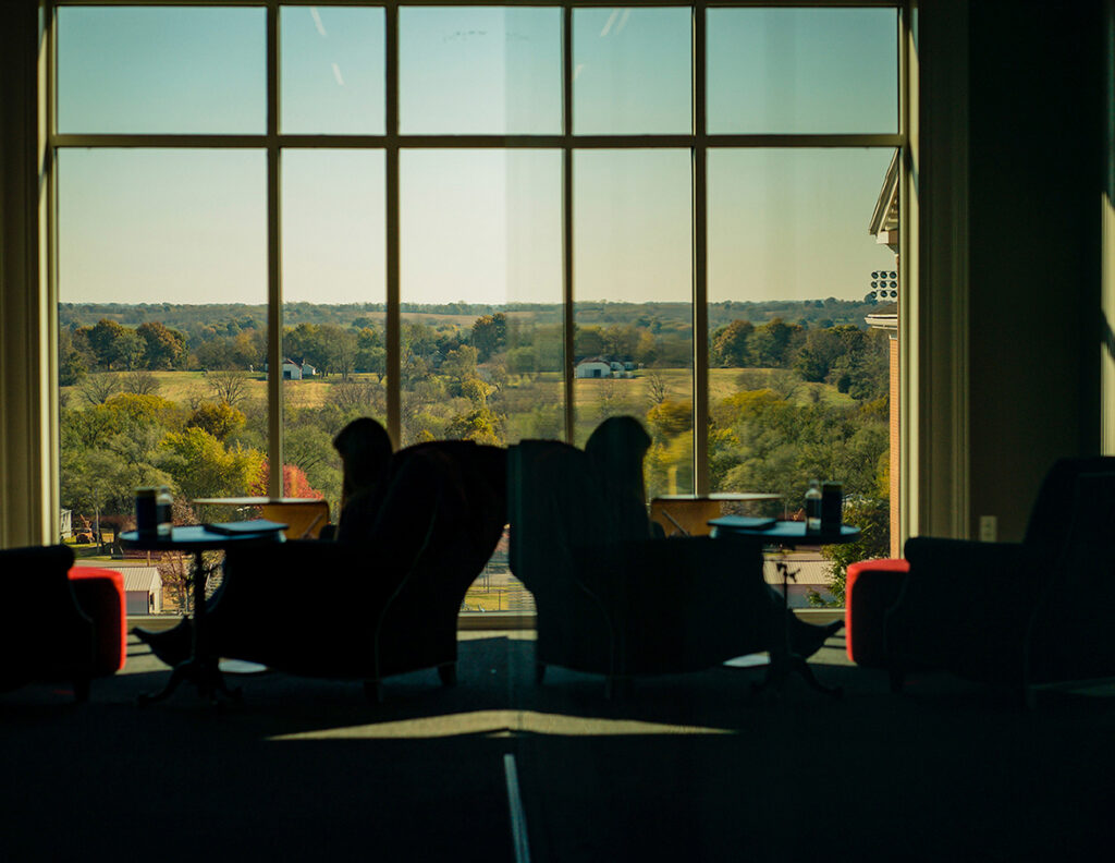 2 students sitting in chairs reading by window in Pryor Learning Commons