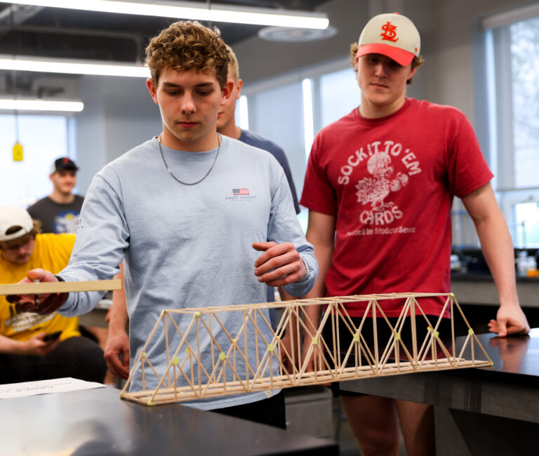 2 engineering students testing weight of balsa bridge model