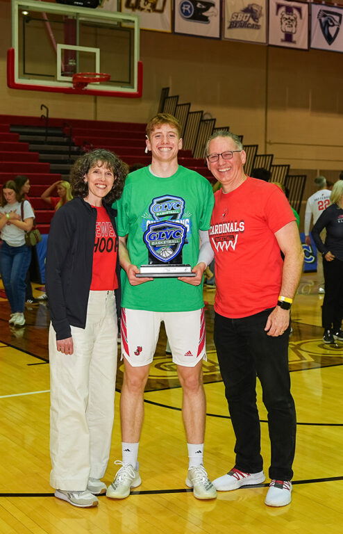 mens basketball player holding conference trophy, posing with parents on court