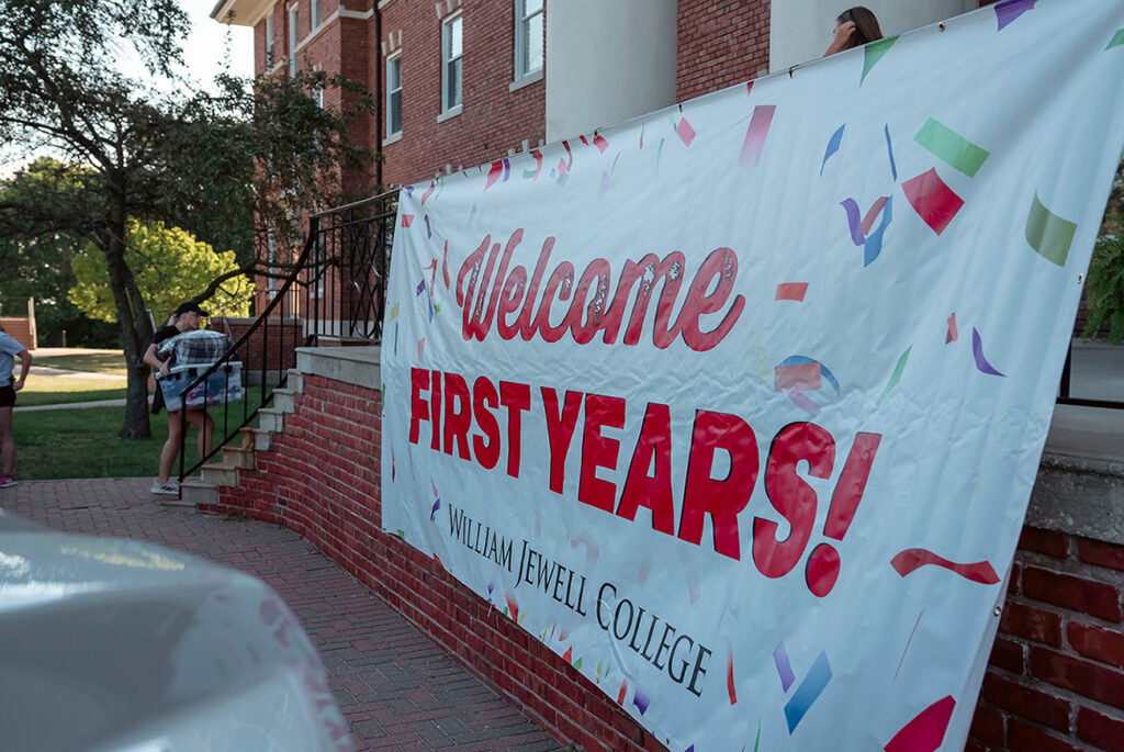 student carrying boxes into residence hall past Welcome banner