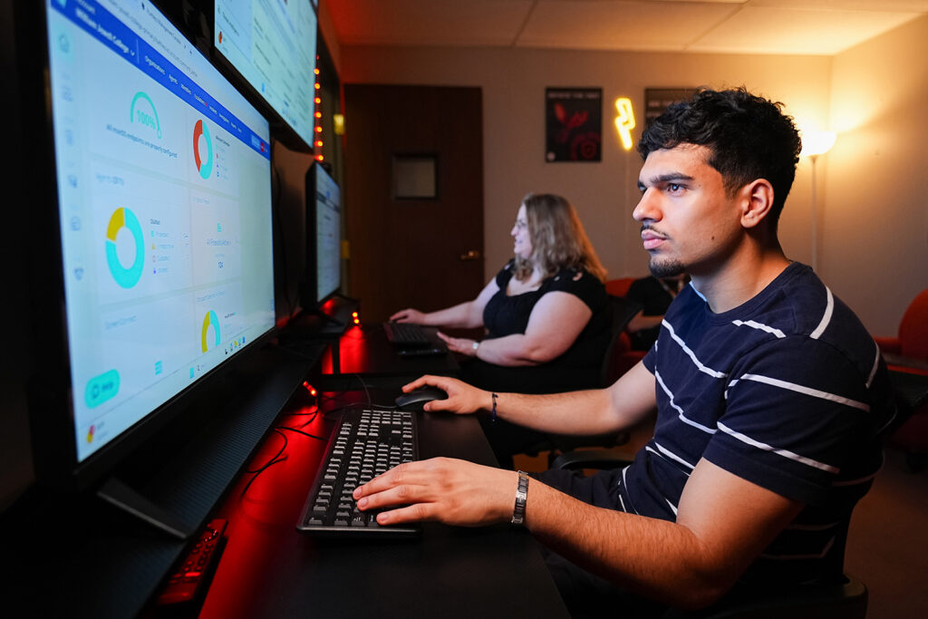 2 cybersecurity students looking at large monitors in a security operations lab