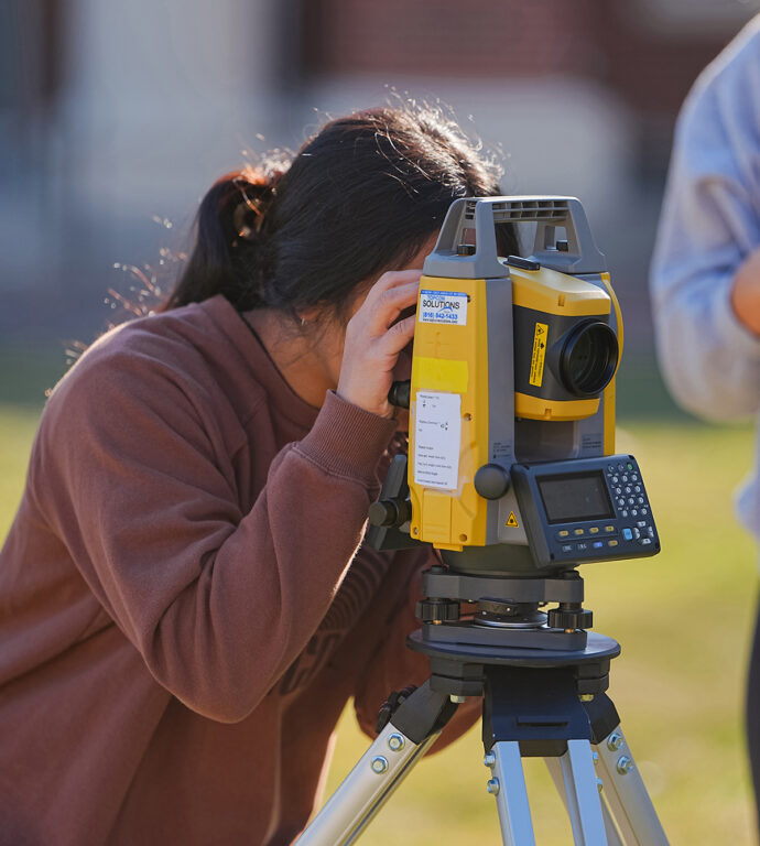 female engineering student looking through land survey camera