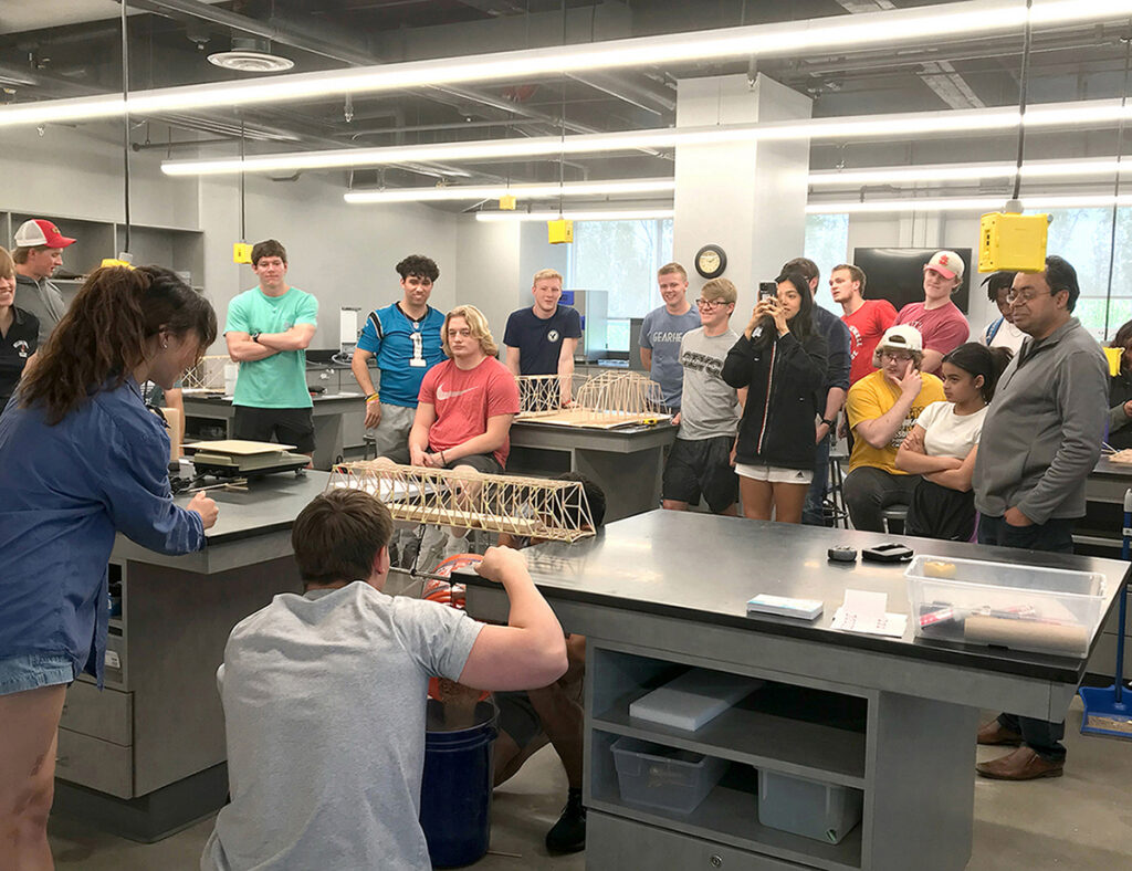 engineering class watching student test balsa bridge model