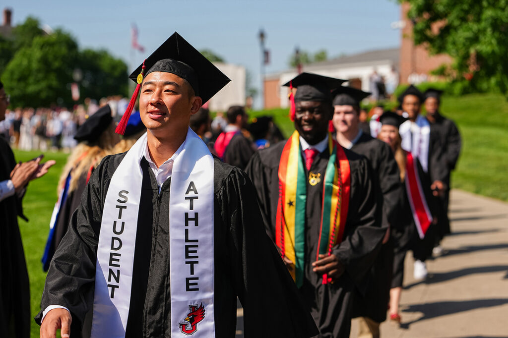grads in caps and gowns walking in line outside