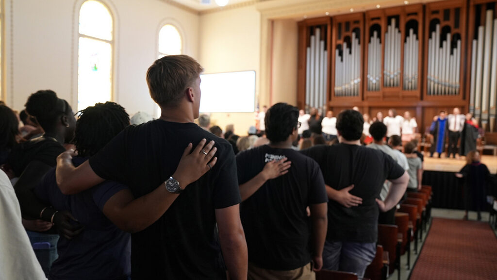 new students arm locked, singing alma mater in chapel during orientation
