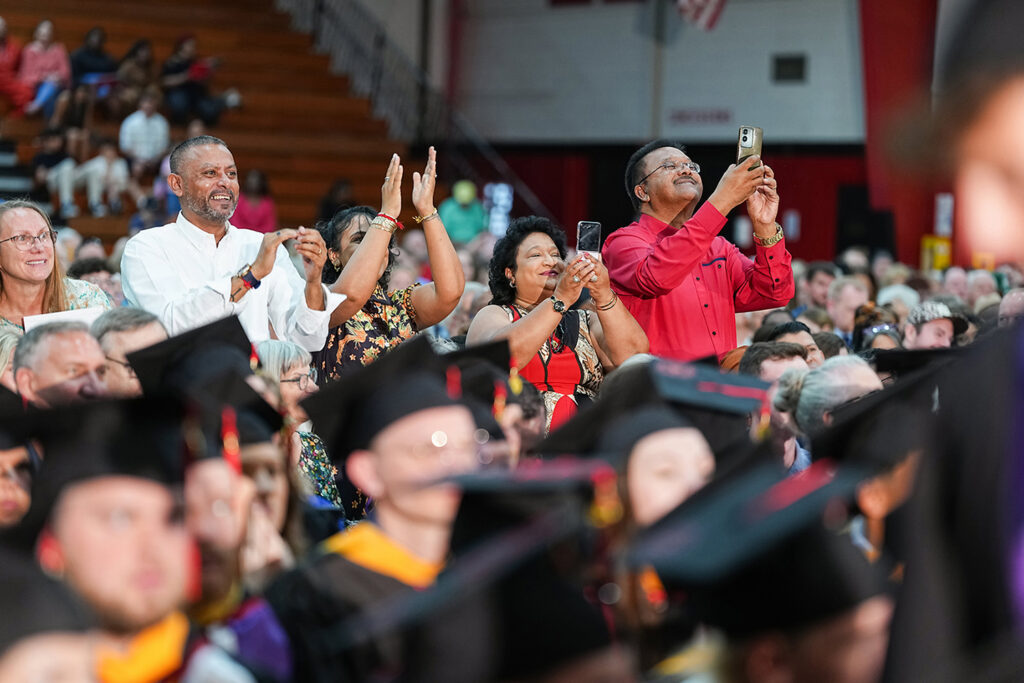 row of parents at commencement, clapping and taking photos of grads