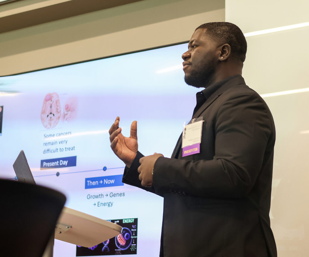 male student at a lectern in a classroom, in front of a presentation on a screen
