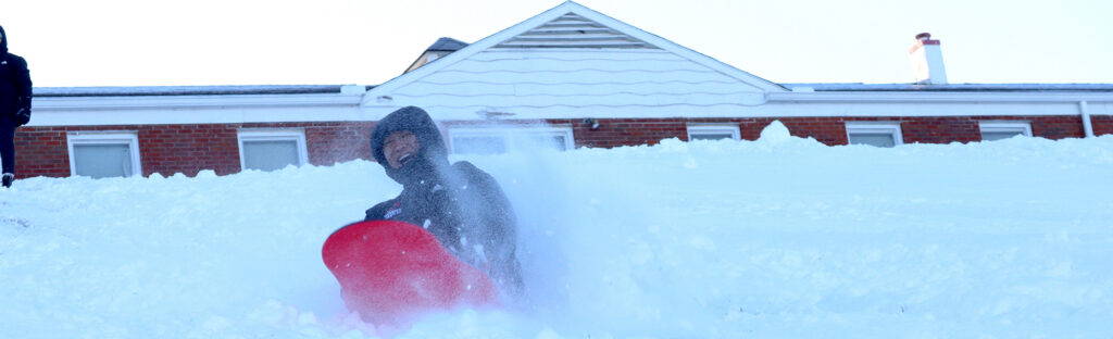 girl sliding down snow covered hill on a sled
