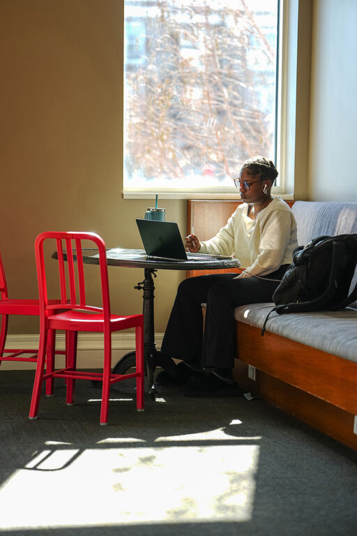 woman at table in library, reading laptop screen