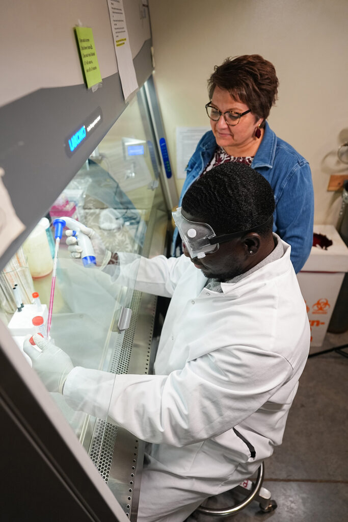 professor observing student in biology lab working under a hood
