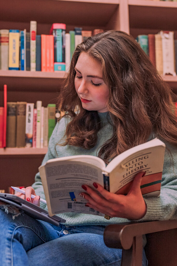 student holding book and looking at iPad in front of bookcase