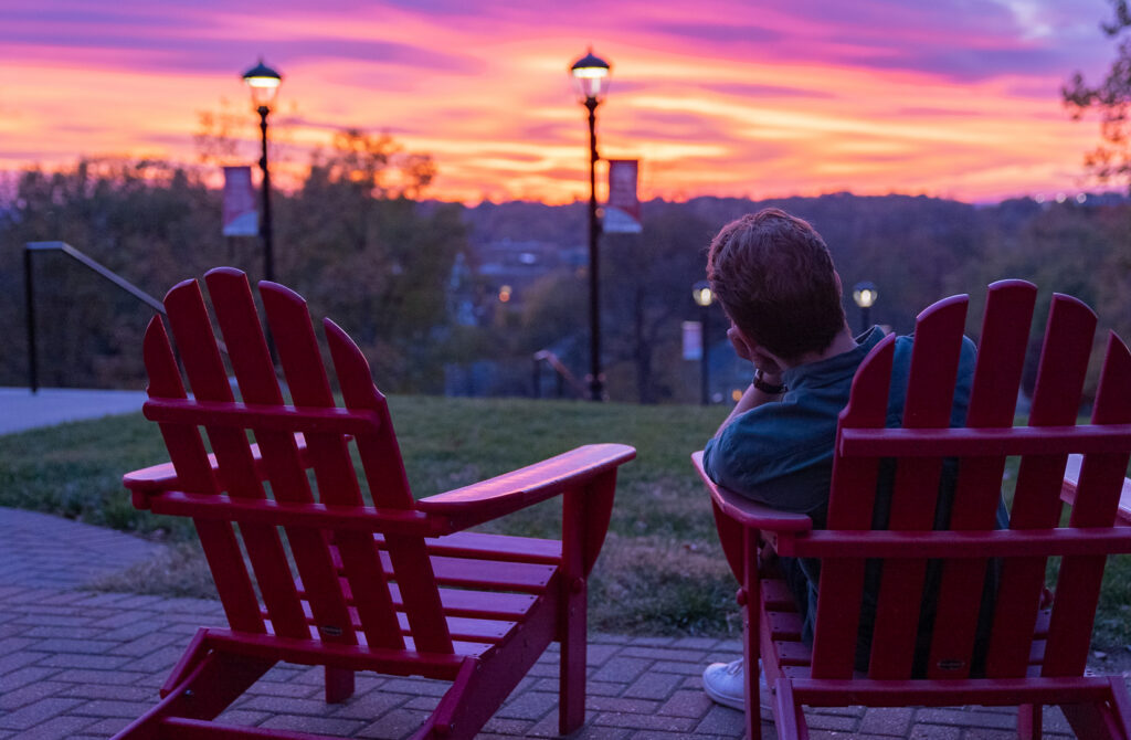 student sitting on campus hillside gazing at the sunset