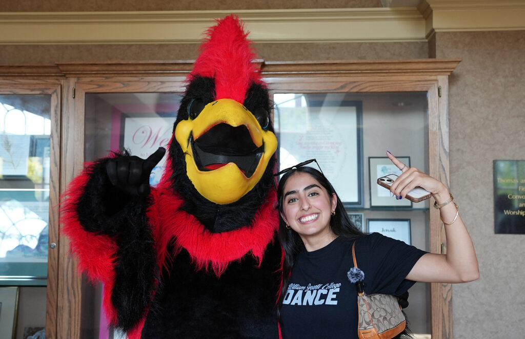 student posing with Cardinal mascot