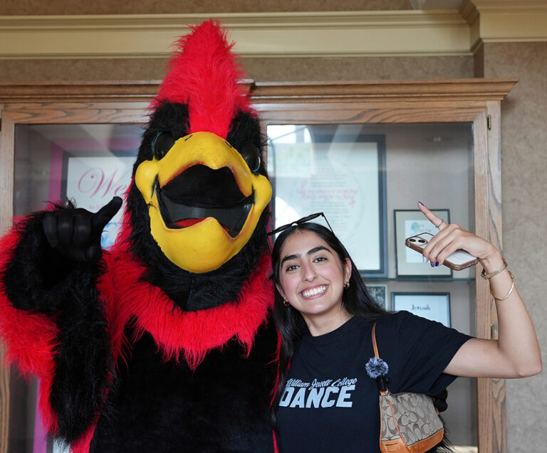 student posing with Cardinal mascot