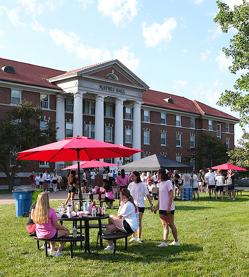 students at tables with umbrellas on Mathes Hall lawn