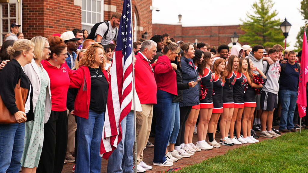 line of students, staff armlocked, singing at pep rally