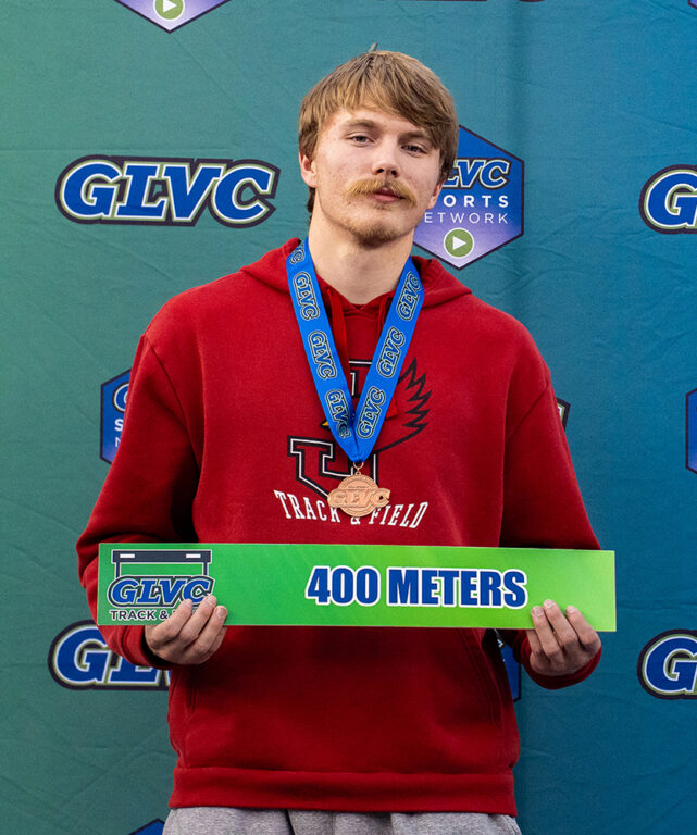track conference champion posing, wearing gold medal