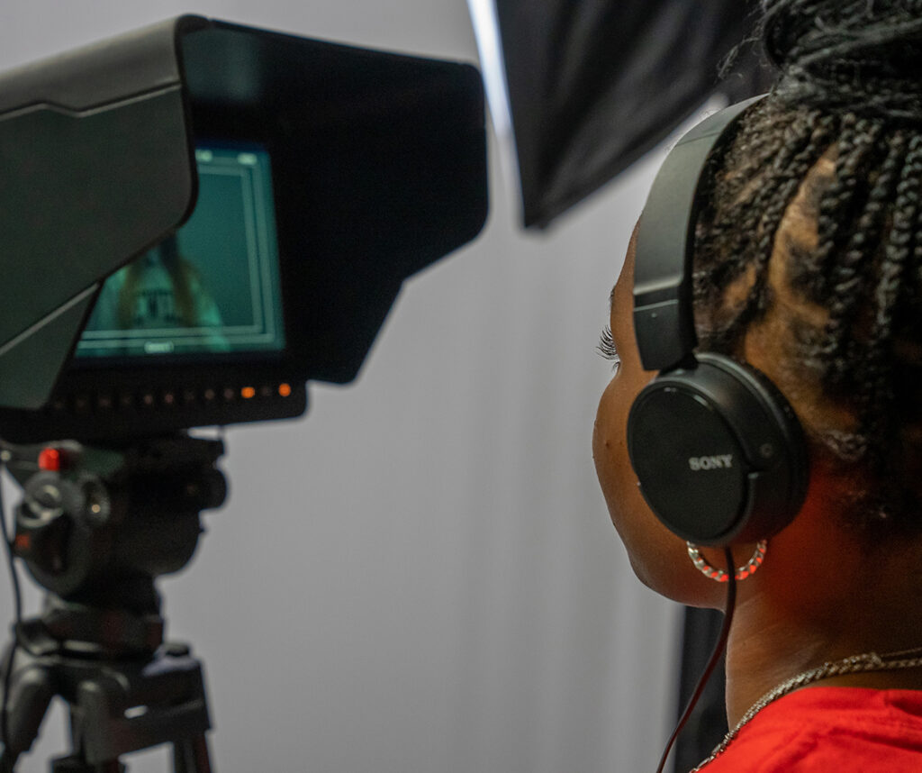 student wearing headset looking into video recording camera in a studio