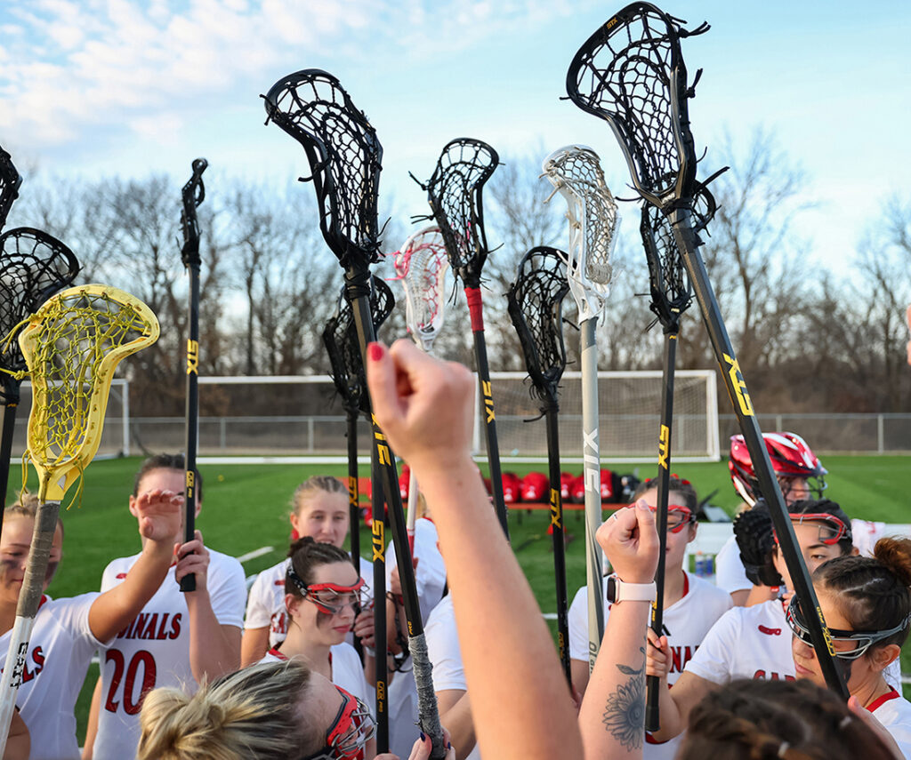 women's lacrosse team in huddle holding up sticks